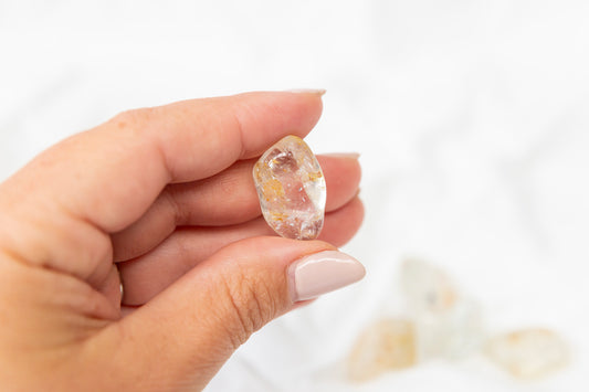 Hand holding a yellow hematoid topaz crystal against a white background