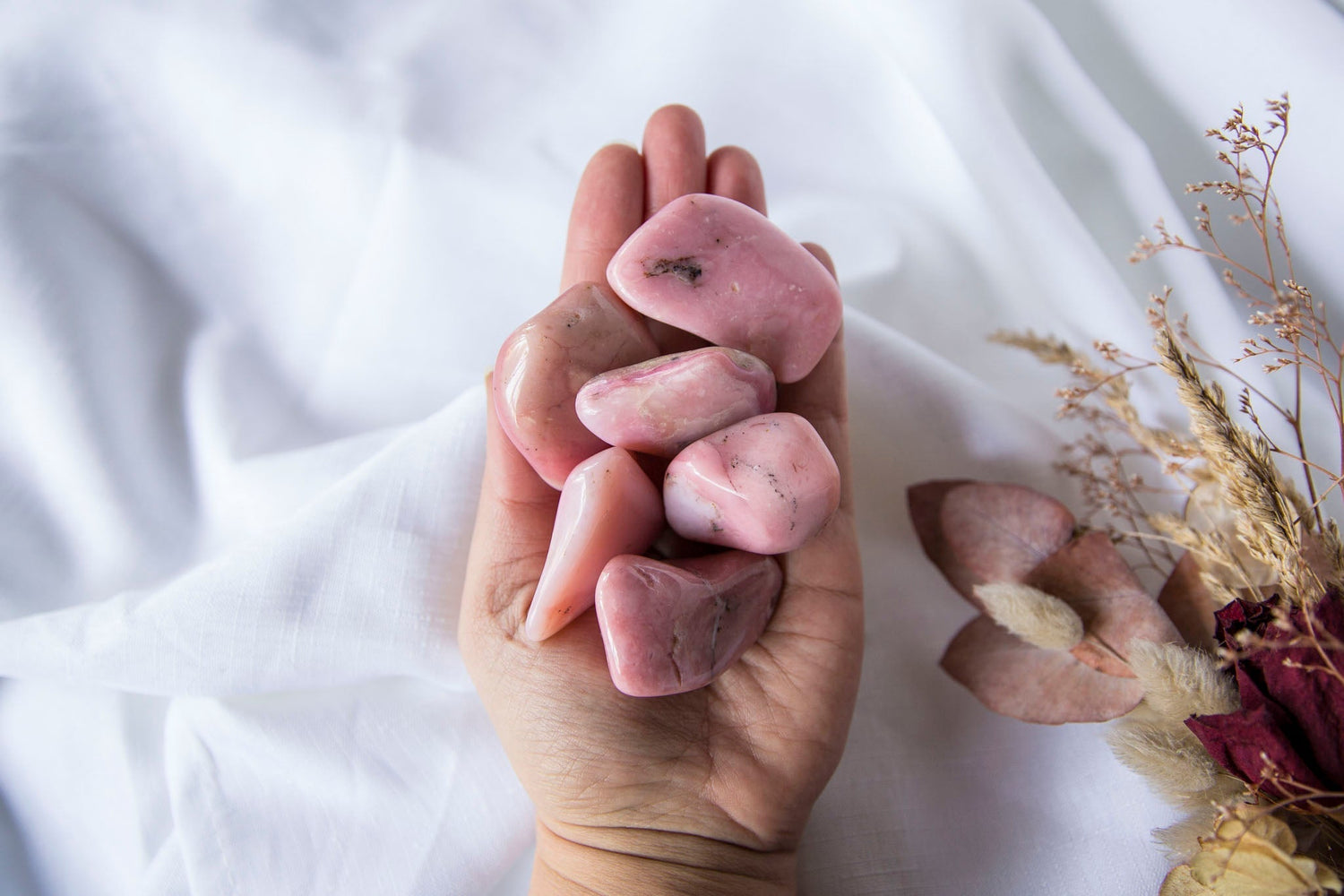Hand holding pink opal tumblestones on a white fabric backgound