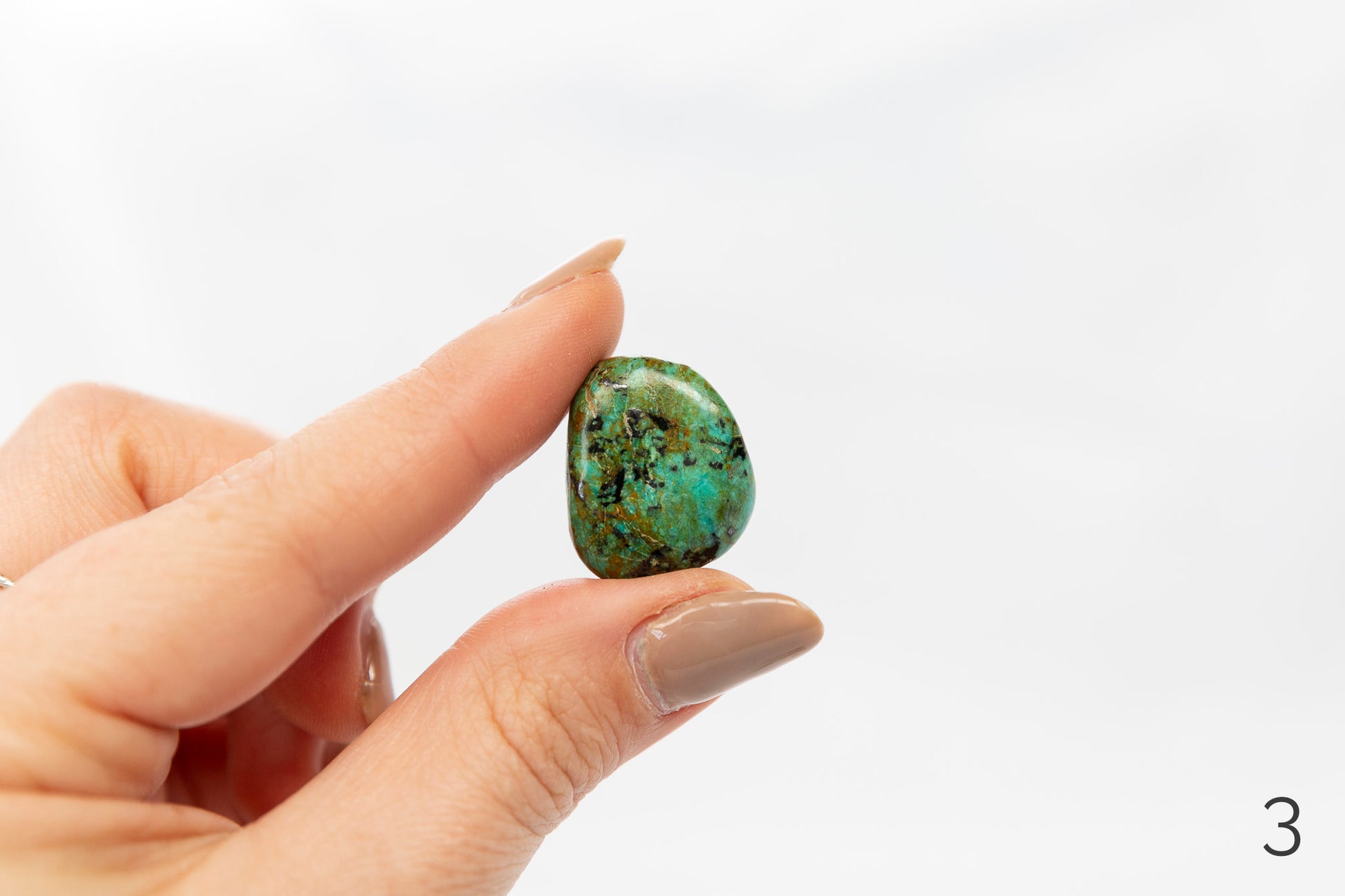 Hand holding a turquoise crystal against a white background