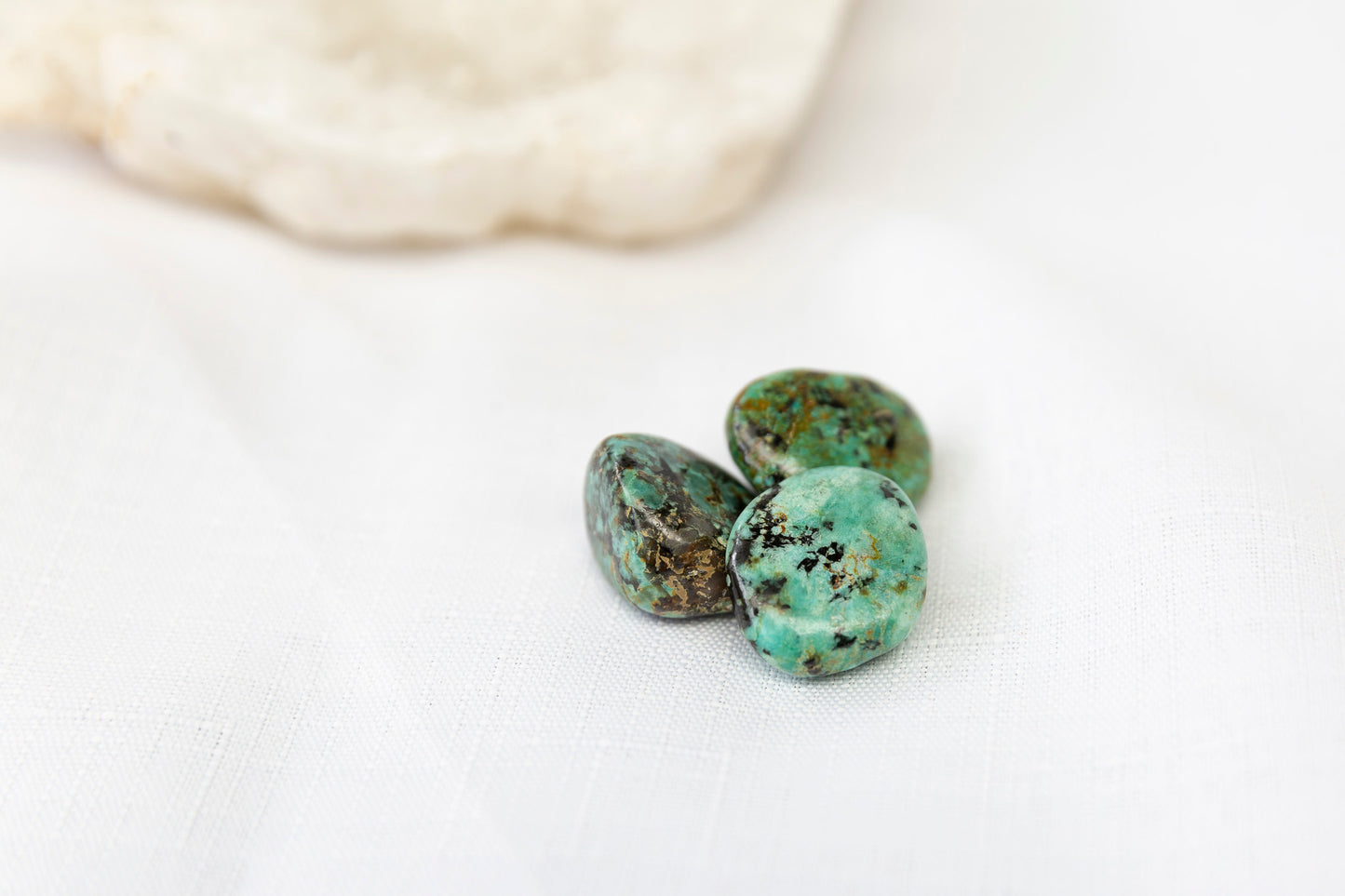 Three turquoise stones on a white surface with a blurred rock in the background