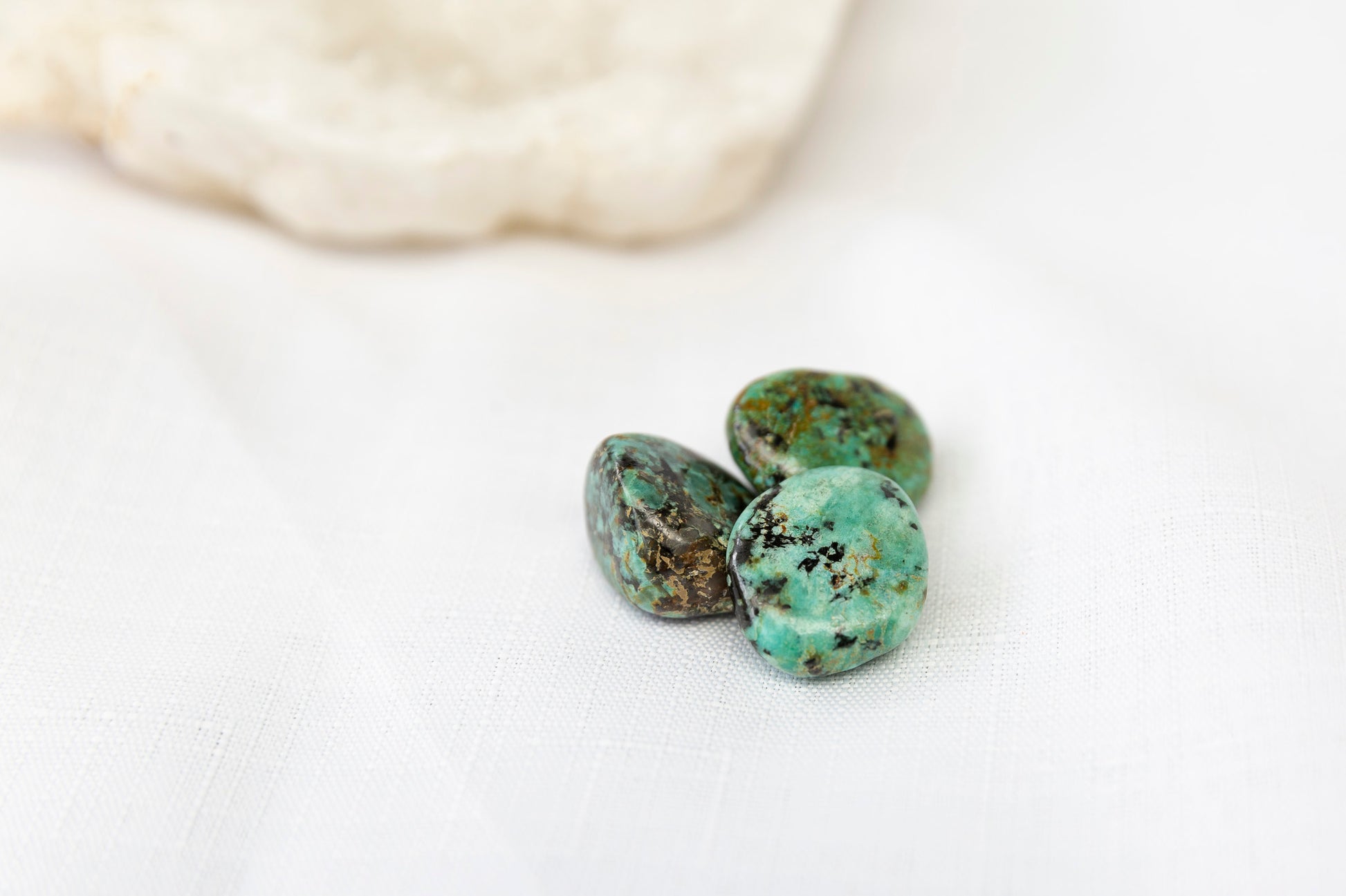 Three turquoise stones on a white surface with a blurred rock in the background