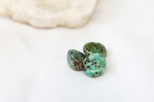 Three turquoise stones on a white surface with a blurred rock in the background