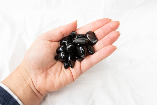 Hand holding a small pile of black apache tear tumblestones against a white background