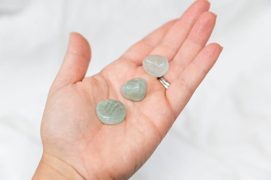 Hand holding three green aquamarine tumblestones against a white background