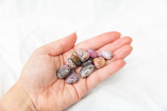 Hand holding small cobaltoan calcite crystal tumblestones against a white background