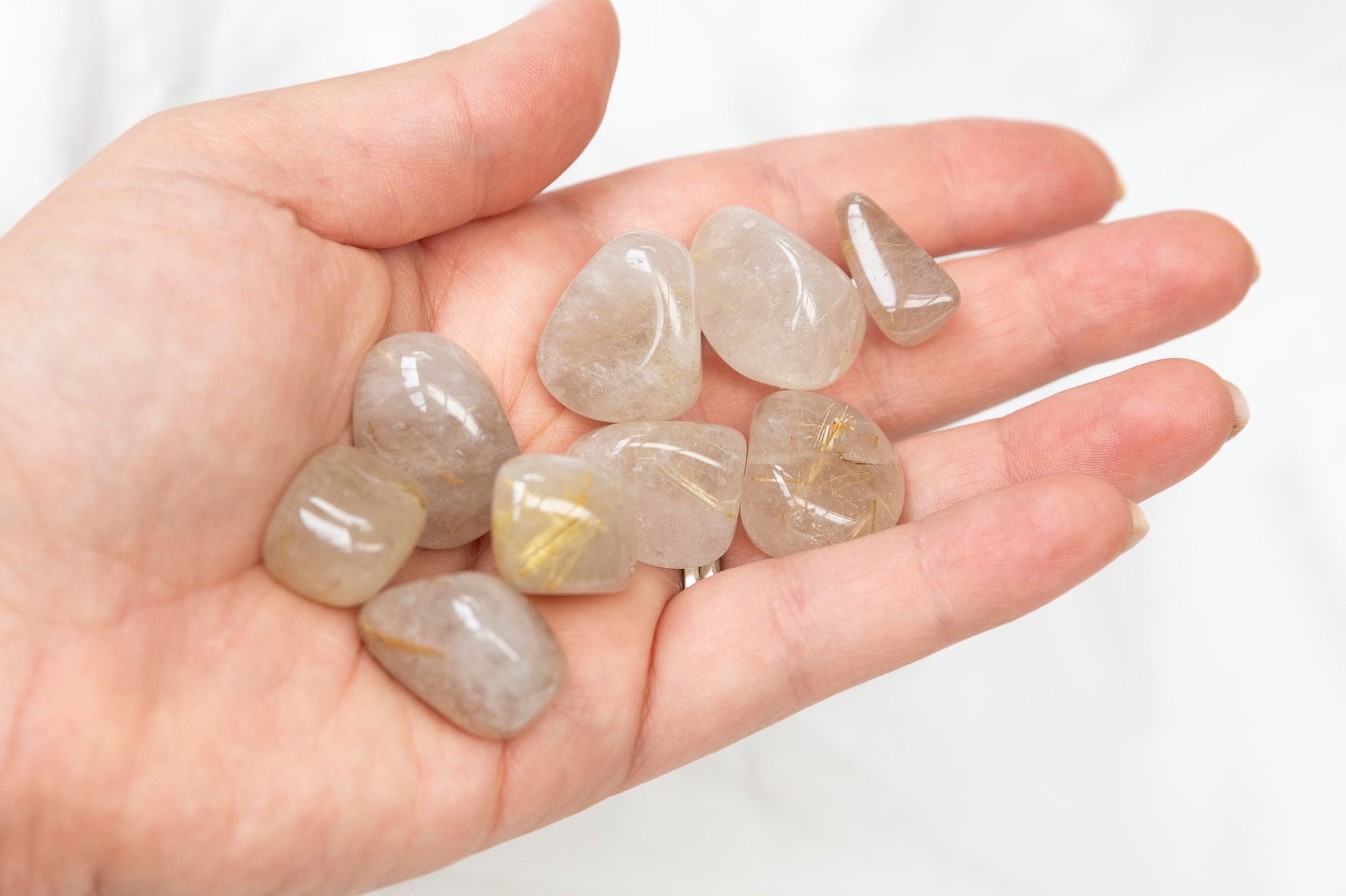 Hand holding a collection of golden rutile quartz tumblestones against a white background
