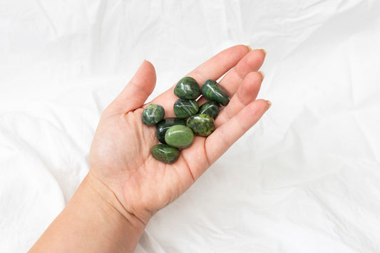 Hand holding green jade crystal tumblestones against a white background