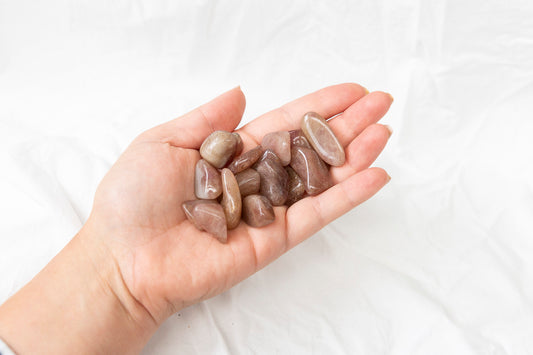 Hand holding a small pile of red aventurine crystal tumblestones against a white background