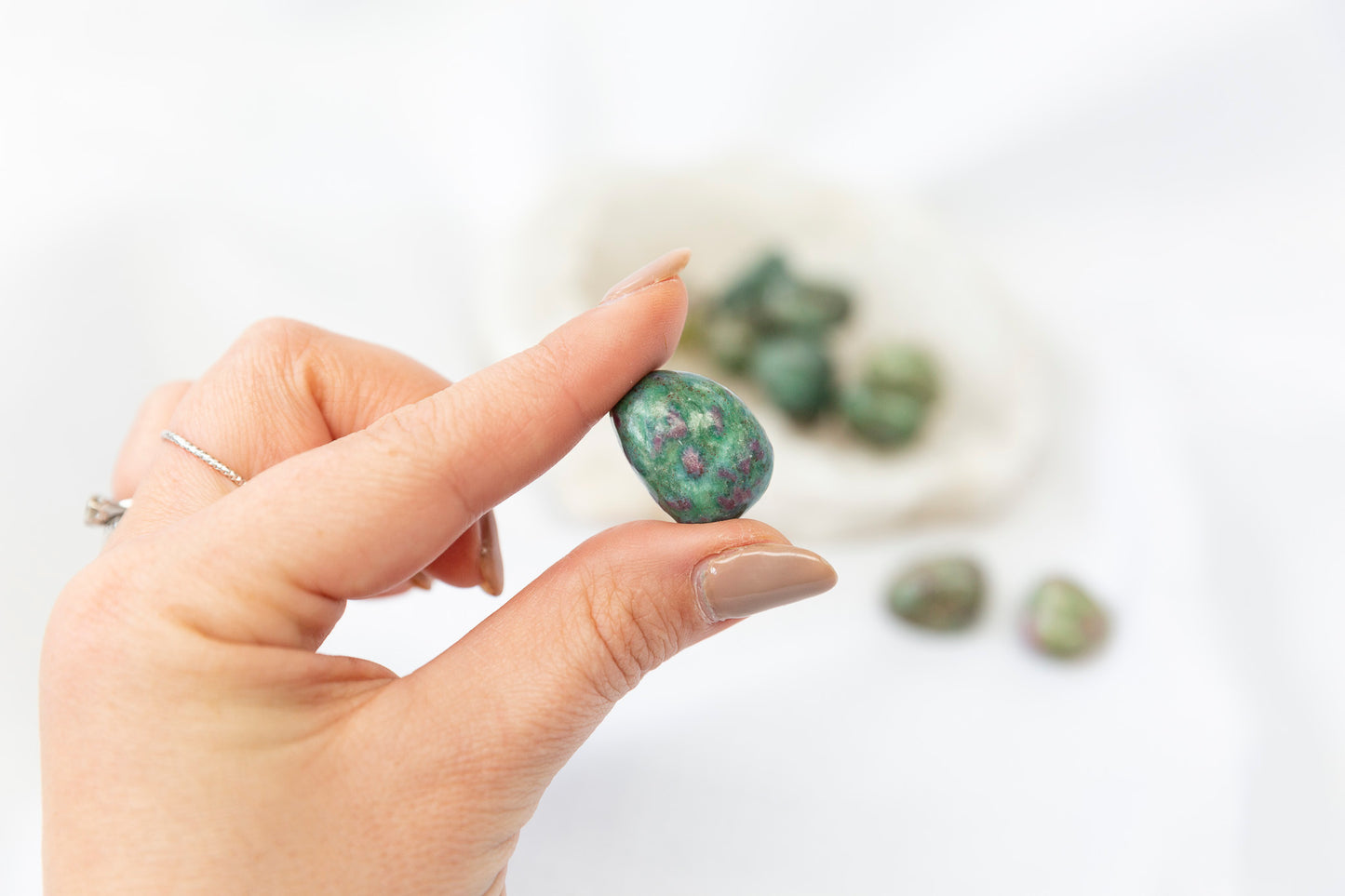 Hand holding a small, pink and green ruby fuchsite tumblestone against a blurred background