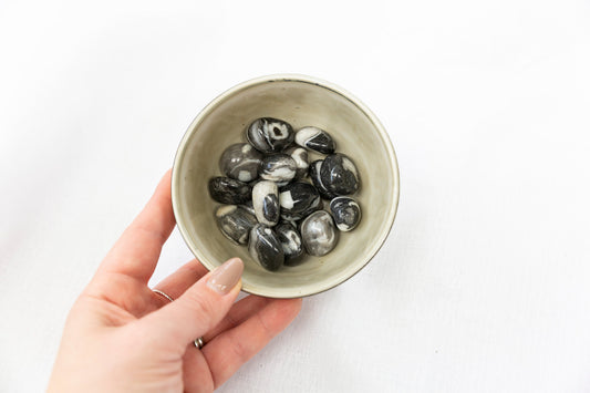 Hand holding a bowl of black and white stones on a white background