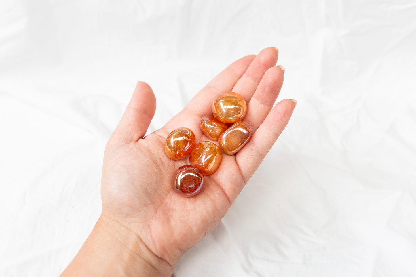 Hand holding tangerine aura quartz tumblestones against a white background