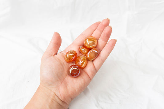 Hand holding tangerine aura quartz tumblestones against a white background