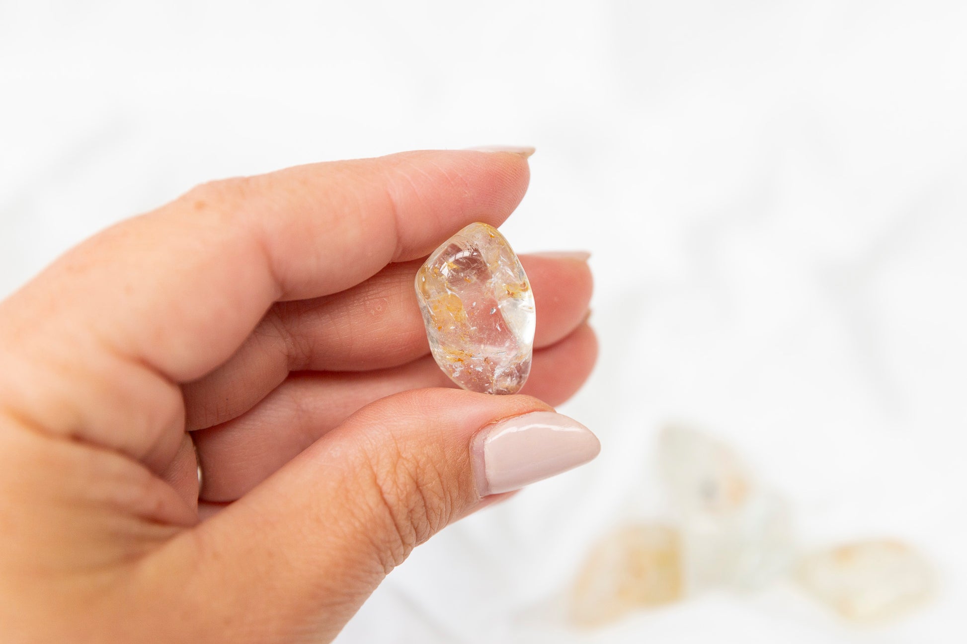 Hand holding a yellow hematoid topaz crystal against a white background