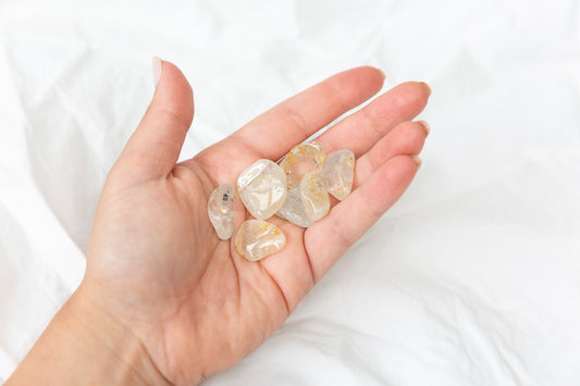 Hand holding several yellow hematoid topaz crystal tumblestones against a white background