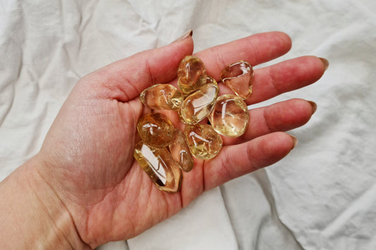 Hand holding natural citrine crystal tumblestones against a white fabric background