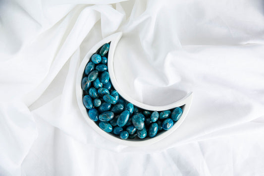A collection of blue apatite tumblestones arranged in a crescent shape on a white, silky surface.