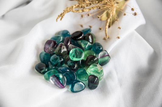A selection of polished Fluorite tumblestones in various shades of blue and green, placed on a white fabric surface.