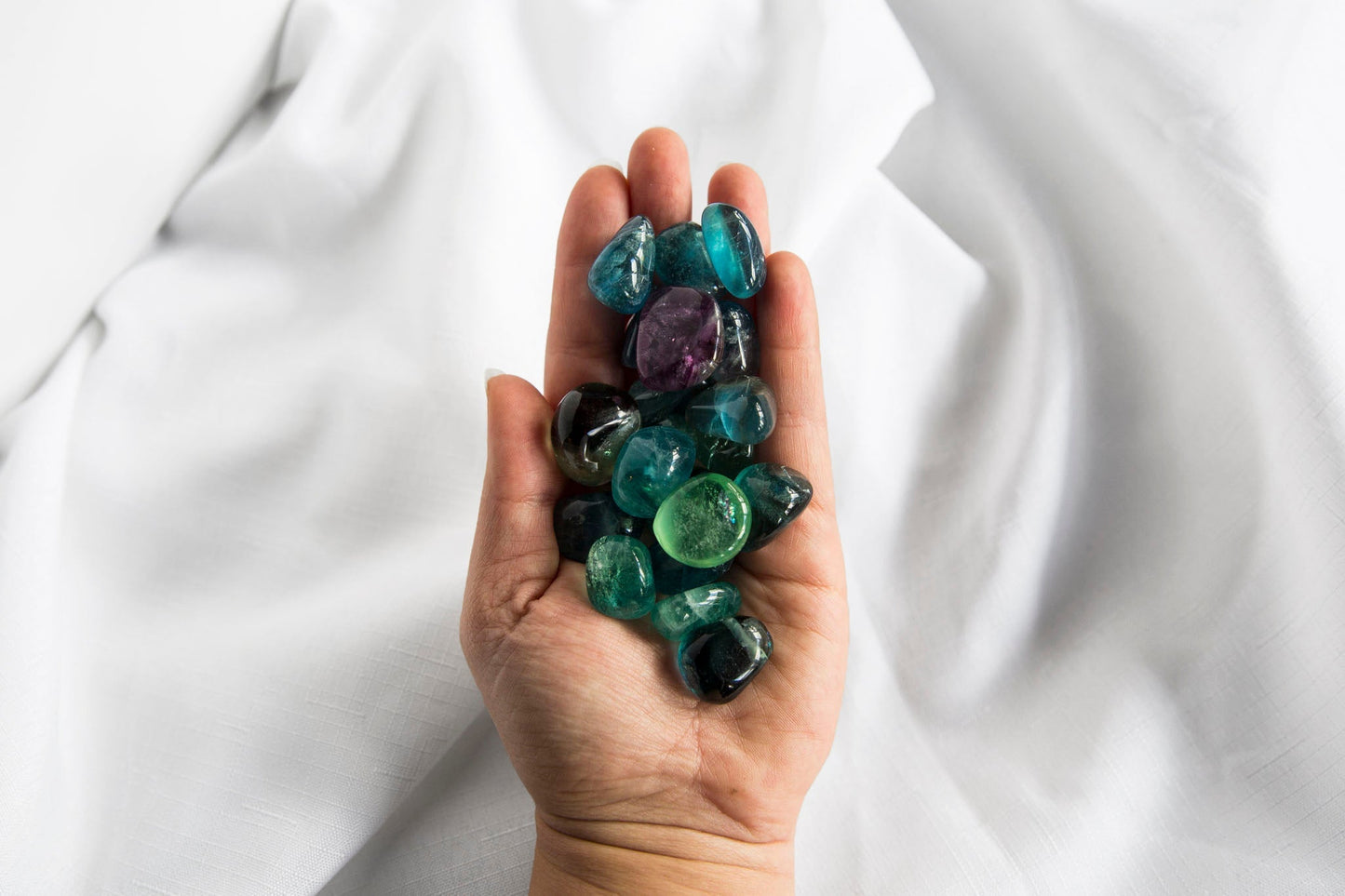 Hand holding fluorite tumblestones on a white background